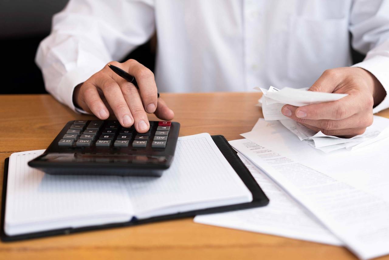 Homem de camisa branca fazendo contas em uma calculadora