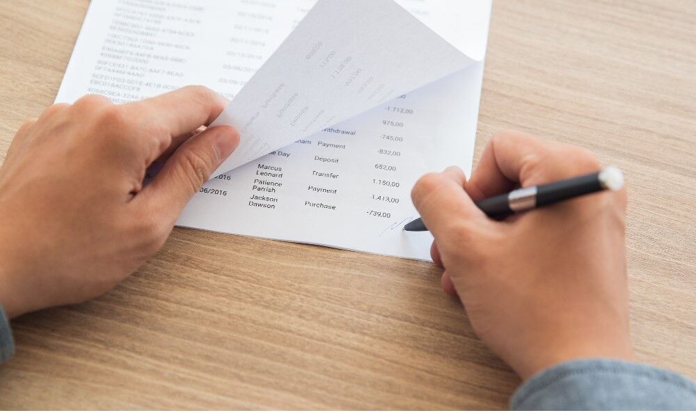 Pessoa revisando documento financeiro em mesa de madeira