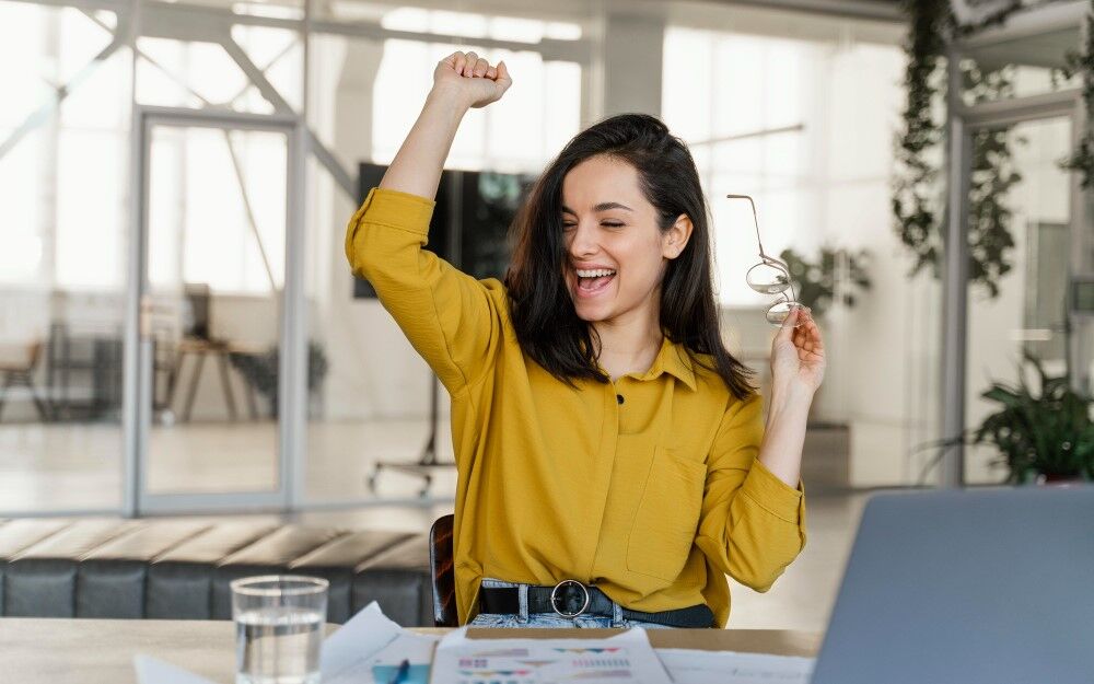 Mulher feliz comemorando sucesso em ambiente de trabalho.